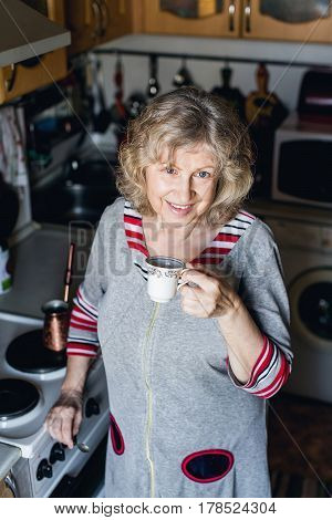 Elderly woman smiling holding Cup of coffee in her kitchen