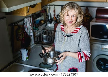 An elderly woman in the home stands at the stove, preparing to cook