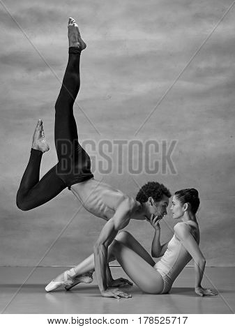 Couple of ballet dancers posing over gray background. Colorless image