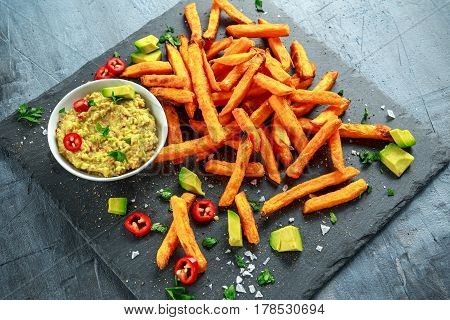 Healthy Homemade Baked Orange Sweet Potato Fries with guacamole, salt, pepper on stine, stone board.
