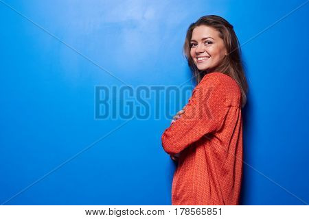 Half-turned portrait of an exhilarated young female standing against blue background. Studio shot of pretty girl isolated 