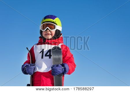 Close-up portrait of happy kid boy holding skis in his hands against blue sky