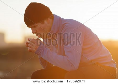 A Young Man In Sports Clothes Resting After Jogging, Trying To Regain Breath And Warm His Palms
