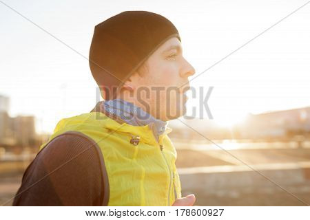 A Young Man In A Hat And Bright Jacket Runs In The Morning At Sunrise. Play Sports And Lead An Activ