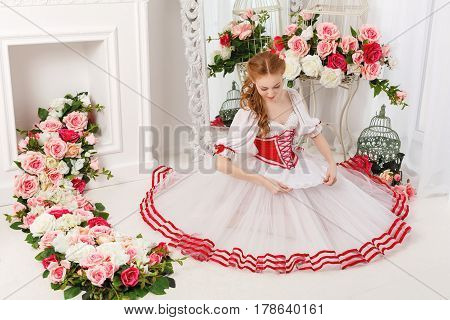 Sweet ballerina in a scenic costume and bouquets of spring flowers. Retro dress. She sits on the floor