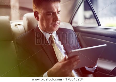 Businessman using digital tablet on backseat of the car