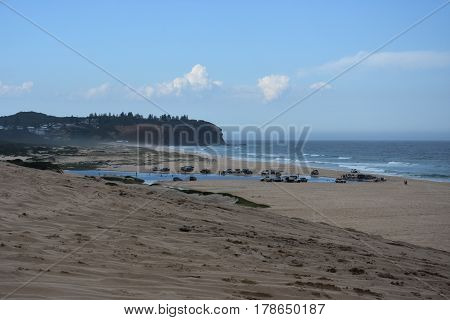 Horizontal landscape of the beach with cars. 4wd cars at Crokers creek (Belmont - Nine Miles - Beach NSW Australia). Redhead Point in the background.