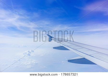 Looking thru airplane 's window seeing wing of airplane white clouds and blue sky