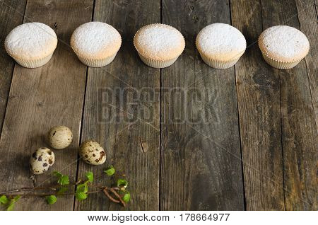 Row of five muffins and quail eggs on an aged wooden background. With space to write a text.