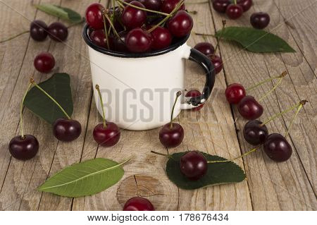 Background of ripe cherries. Pile of fresh and tasty cherries in emal cup. Fresh cherries scattered on a wooden table. Top view.