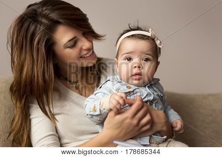 Young mother holding her baby girl in her lap playing and enjoying motherhood. Focus on the baby