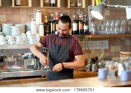 small business, people and service concept - happy man or waiter in apron with holder and tamper preparing espresso at coffee shop