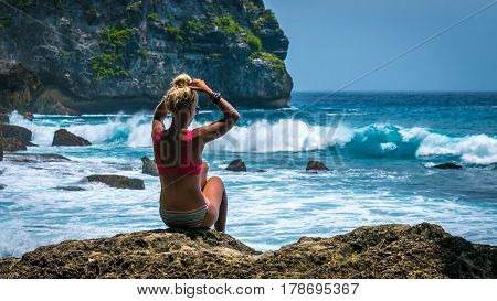 Girl sitting on the Rock and watching Huge Waves hitting Tembeling Coastline at Nusa Penida Island, Bali Indonesia.