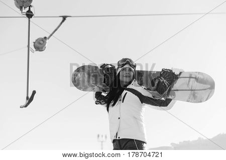 Black and white photo of long-haired female athlets in ski suit with snowboard on mountain slope