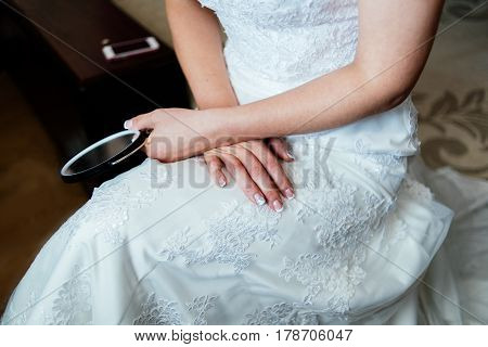 Bride in white wedding dress is sitting and holding a mirror