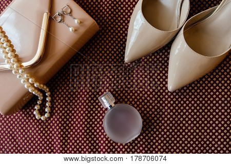 Bride's shoes perfume necklace and clutch are on burgundy cloth surface