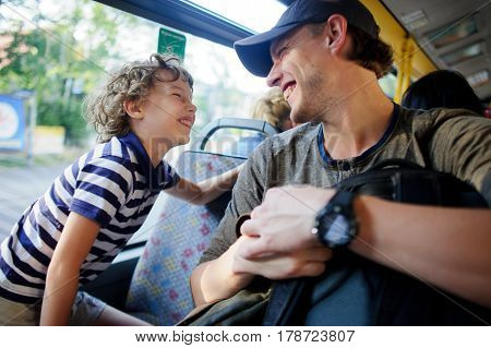The young man goes by the bus together with the son. The father and the son sit next with each other and communicate with pleasure. On their faces expression of love and joy.