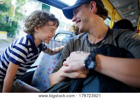 The young man goes by the bus together with the son. The father and the son sit next with each other and communicate with pleasure. On their faces expression of love and joy.