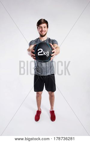 Handsome hipster fitness man in gray t-shirt holding medicene ball. Studio shot on gray background.