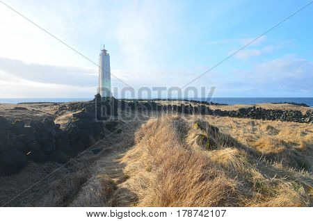 Lighthouse Malarrif amongst lava rocks and tall grass in Iceland.