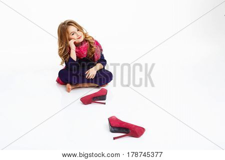 Girl sitting on floor shoeless. Kid in elegant clothing looking straight with charming smile.