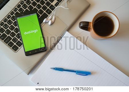 Nitra, Slovakia, march 28, 2017: Duolingo application in a mobile phone screen. Workplace with a laptop, an earphones, notepad and coffee.