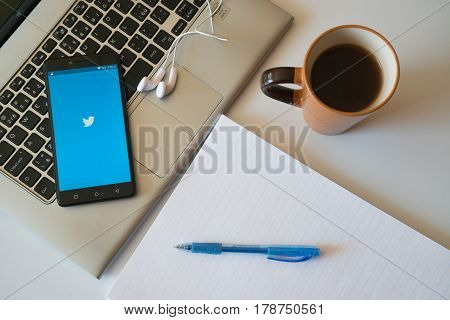 Nitra, Slovakia, march 28, 2017: Twitter application in a mobile phone screen. Workplace with a laptop, an earphones, notepad and coffee.