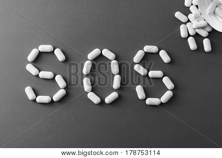 White Pills On Black Background, Which Forming The Word Sos, With A Blister Of Pills On Background.