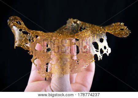 Hand holding a slab of concentrated cannabis oil extraction aka shatter isolated over black background