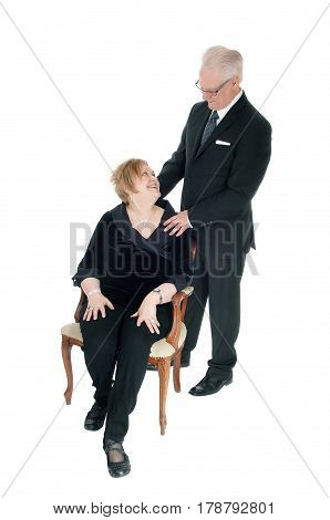 A nice senior citizen couple she sitting in an old armchair he standing behind her his hands on her shoulder isolated for white background.