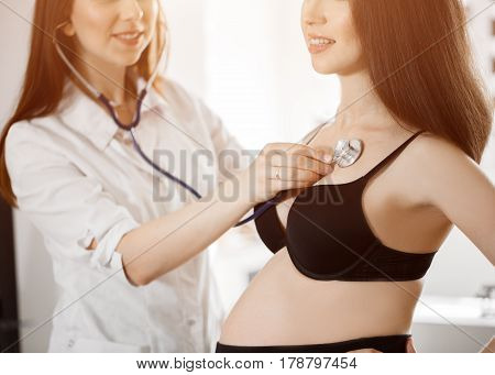 Female Medicine Doctor Holding Stethoscope To Pregnant Woman Standing For Encouragement, Empathy, Ch