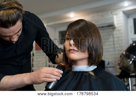 Male hairdresser does a haircut to pretty woman in the beauty salon.