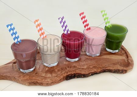 Health food supplement drinks of chocolate whey protein, maca root herb, acai berry, pomegranate fruit and wheat grass on an olive wood board. Also used by body builders.