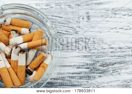 Glass ashtray with cigarette butts on wooden background