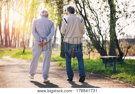 View from behind of an adult son walking with his senior father in the park.