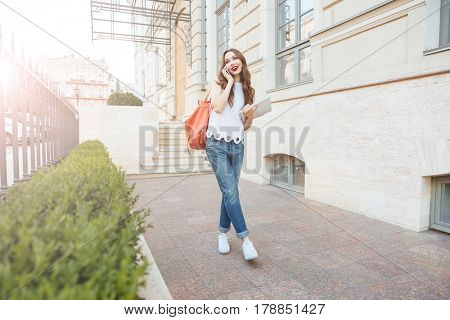Young beautiful brunette girl talking on the phone and walking on the city street