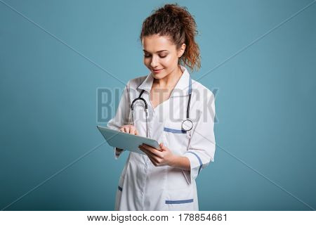Potrait of a smiling female doctor or nurse using tablet pc computer isolated on blue background
