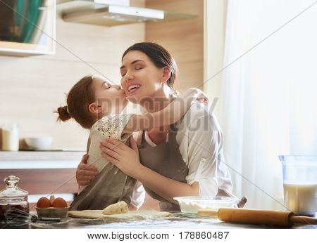 Happy loving family are preparing bakery together. Mother and child daughter girl are cooking cookies and having fun in the kitchen. Homemade food and little helper.