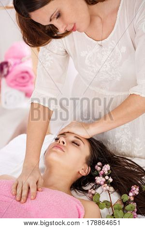 Sideview of messeur doing facial massage on young woman lying on couch with pink flowers