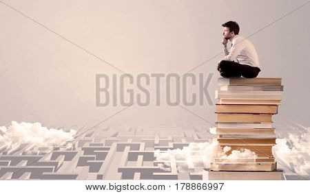 A serious businessman in suit sitting on a pile of giant books in front of a grey wall with clouds, labirynth