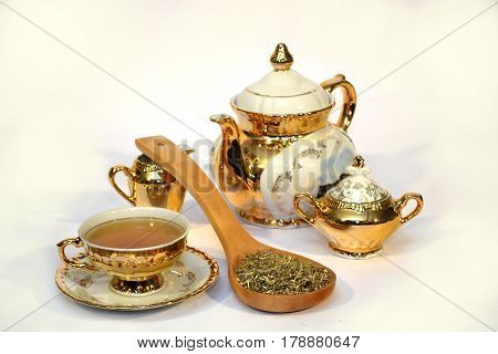 Golden tea set with a spoon full of herbs on white background