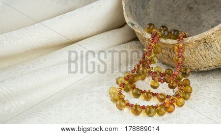 Ancient yellow glass button necklace separated by small red trade beads on a pot and Thai silk background