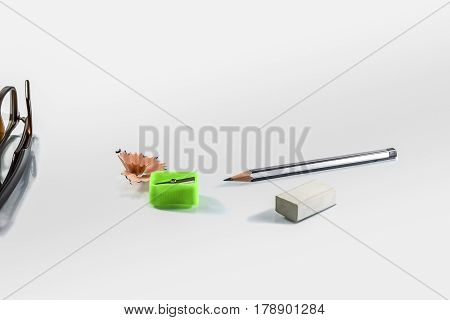 Back to school concept- a Pencilerasor sharpner an cut slice of the pencil on white table with or without spectacles not properly aranged isolated.