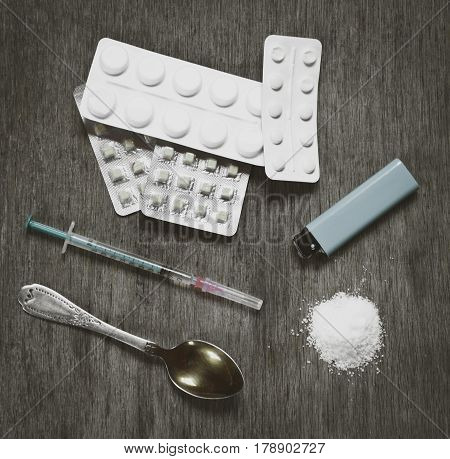 Drug syringe and cooked heroin with drugs pills on the desk