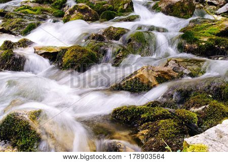 Mountain river background with small waterfalls in tropical forest. Clean blue water flows on cascades of Erawan park in Thailand