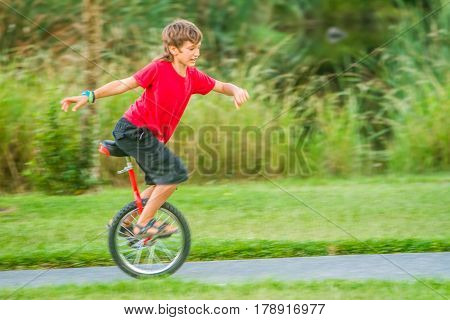 outdoor portrait of young boy riding a unicycle (one wheel bike) on natural background