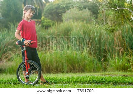 outdoor portrait of young boy riding a unicycle (one wheel bike) on natural background