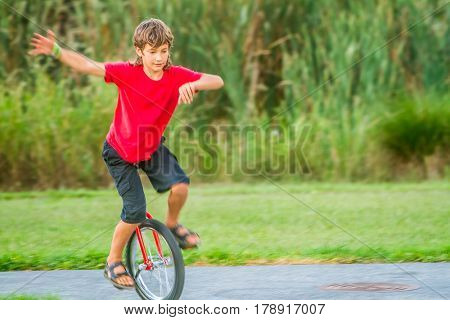 outdoor portrait of young boy riding a unicycle (one wheel bike) on natural background
