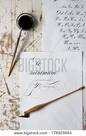 Word Calligraphy written on paper, with calligraphy tools in background. alphabet.