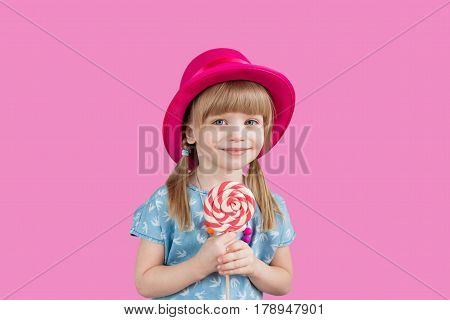 Funny child with candy lollipop, happy little girl eating big sugar lollipop, kid eat sweets. surprised child with candy. isolated on bright background, studio. Beautiful little girl with lollipop